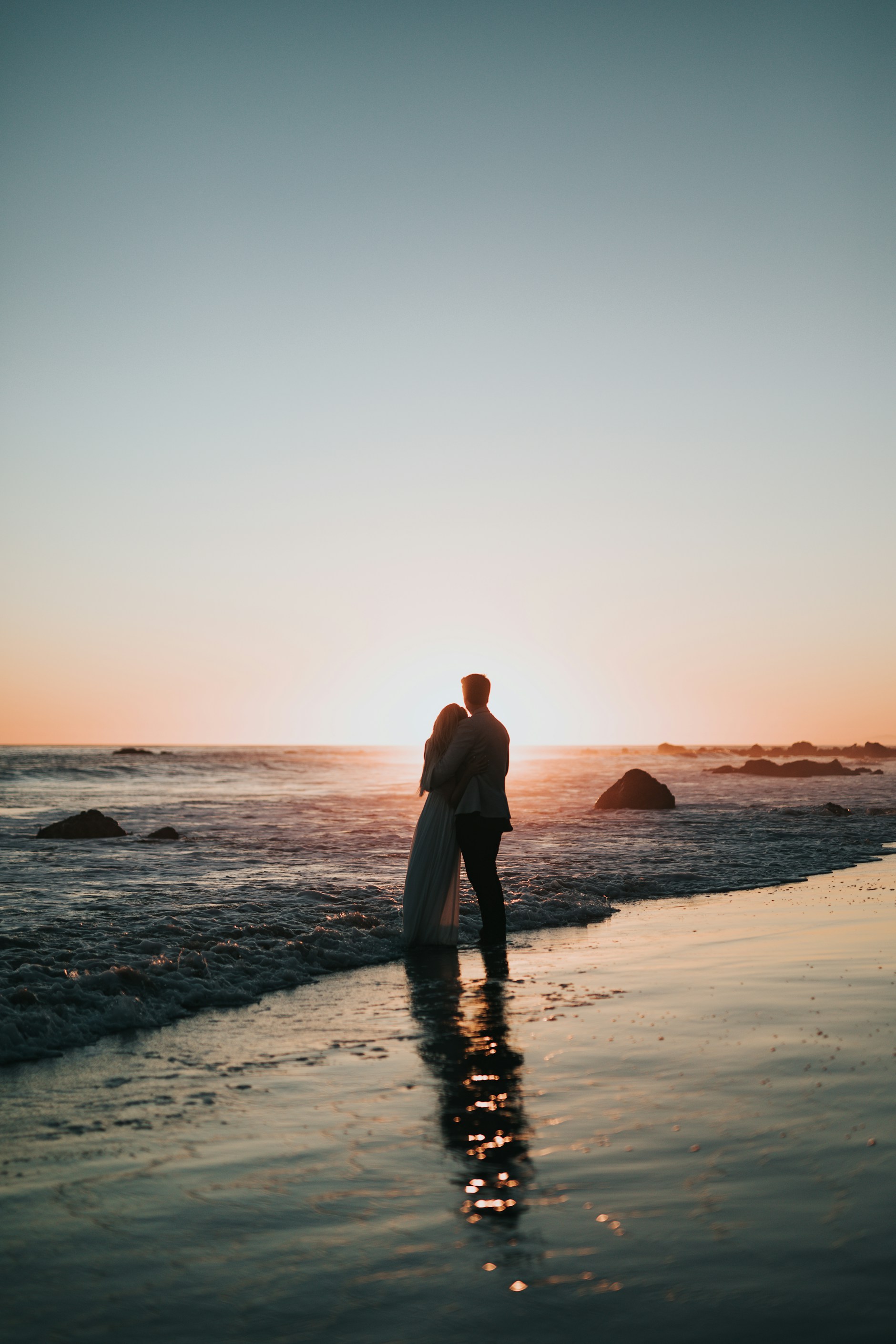 A couple embracing at the water's edge at sunset